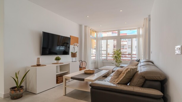 A modern living room with a flat-screen TV, a sofa, a coffee table, and a potted plant. - Two-bedroom apartment with pool and tennis court (Costa Adeje)