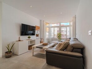 A modern living room with a flat-screen TV, a sofa, a coffee table, and a potted plant.