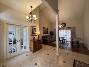 A spacious living area with a high ceiling, a chandelier, a sofa, a dining table, and a foosball table.