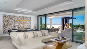 A modern living room with a sectional sofa, a dining area, and a large glass door leading to an outdoor terrace.