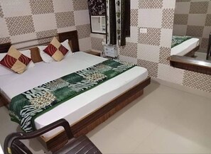 A neatly made bed with a patterned bedspread, a wooden headboard, and a bedside table with a mirror. - Hotel Bharat Residency  (Amritsar)