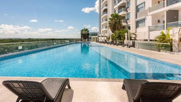 A swimming pool with lounge chairs, a high-rise building, and a clear sky. - Yuum Ha (Cancún)
