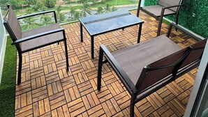 A balcony with wooden flooring, two chairs, a small table, and a green wall. - Yuum Ha (Cancún)