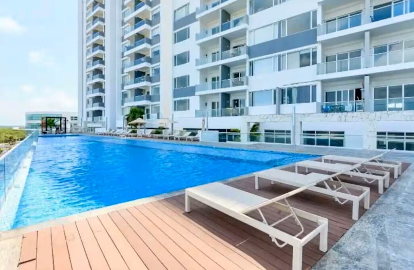 A modern hotel with a large swimming pool, sun loungers, and a wooden deck.