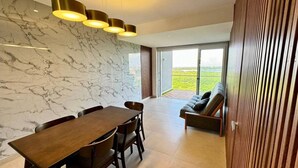 A modern dining area with a marble wall, a wooden dining table, and a sofa with a view of the outdoors. - Yuum Ha (Cancún)