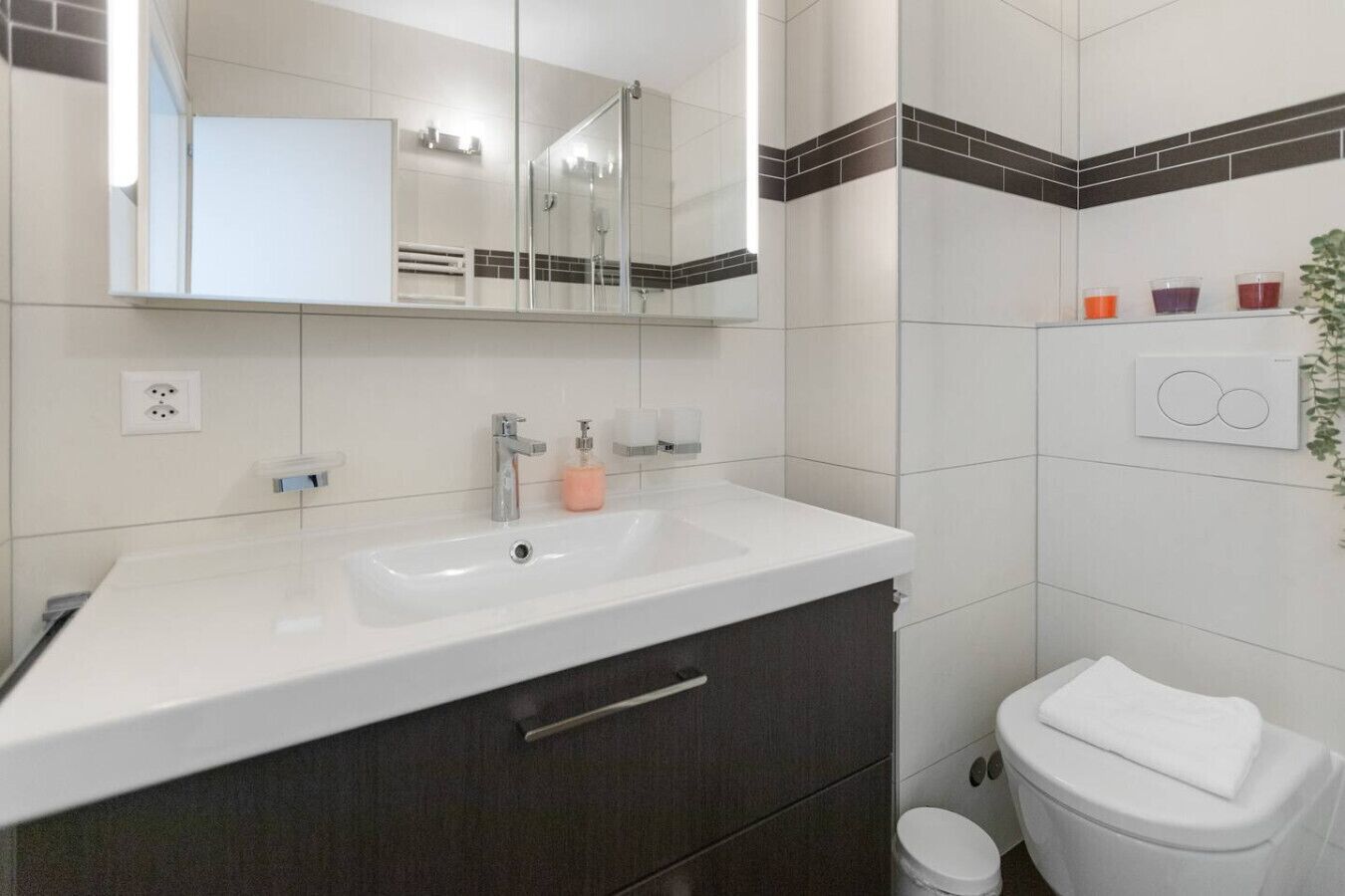 A modern bathroom with a white sink, dark cabinets, a mirror, and a toilet.
