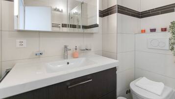 A modern bathroom with a white sink, dark cabinets, a mirror, and a toilet.
