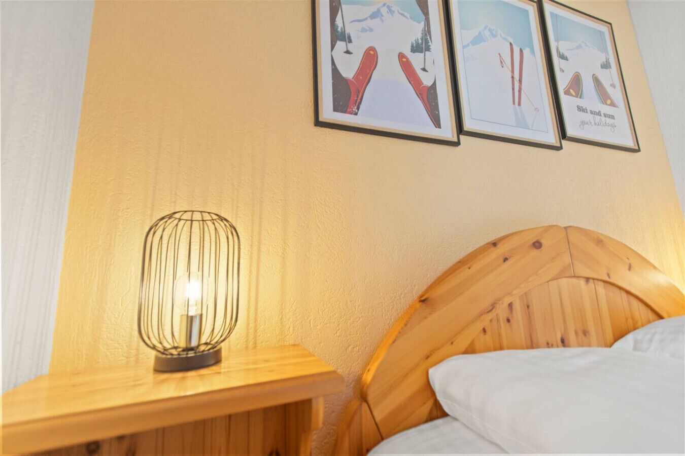 En säng med ett huvudgavel av trä, en vit kudde, ett nattduksbord med en lampa och två inramade tavlor på väggen.