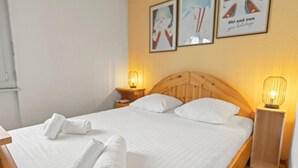 A neatly made bed with white linens and two rolled towels on the side. There are two bedside tables with lamps, and the room has a wooden headboard. - Crans-Montana center : Studio Ski 2 pers (Crans-Montana)