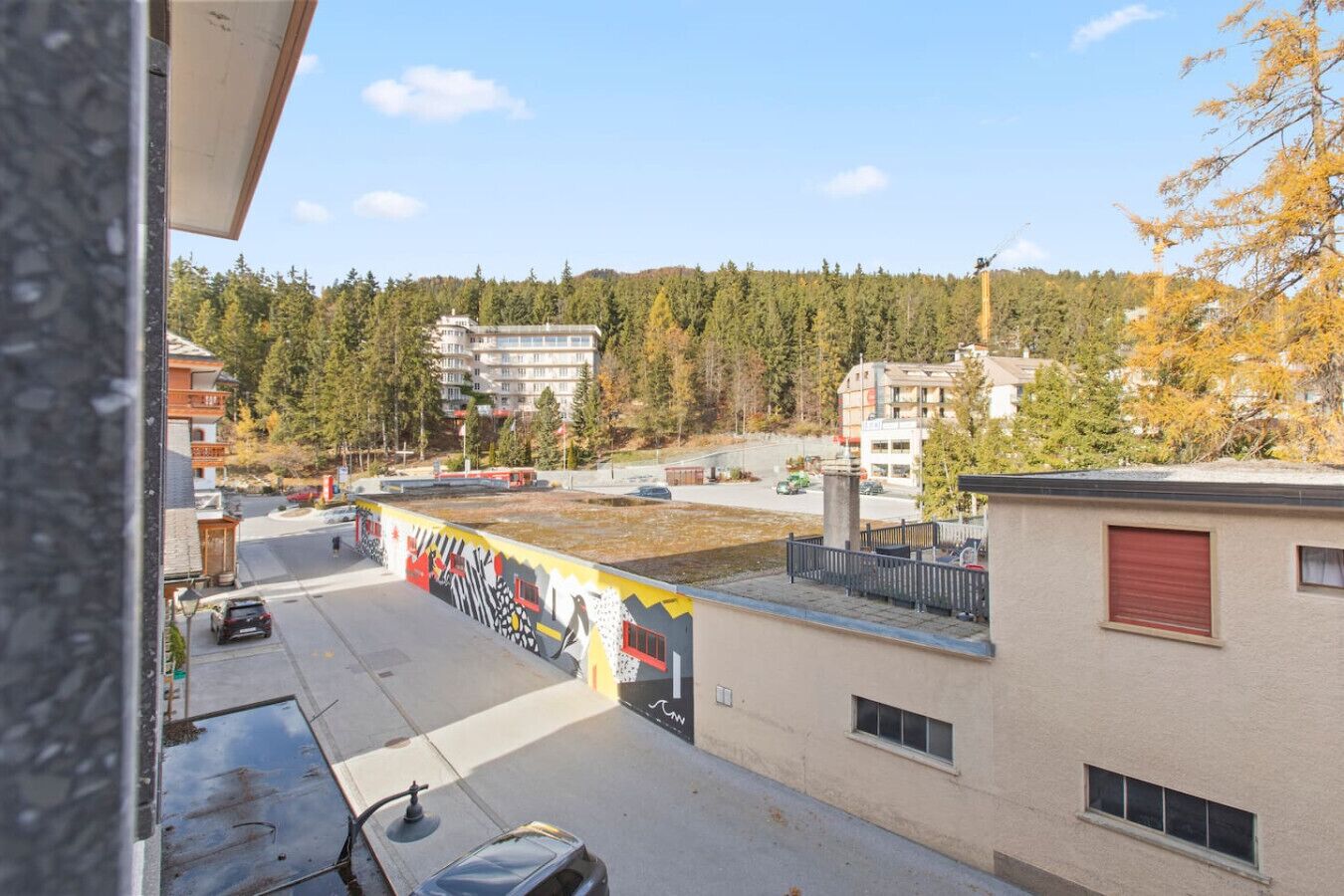 Un edificio con un mural en la fachada, un estacionamiento y vistas a una zona boscosa.