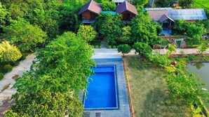 Vista aerea di un resort con piscina circondata da rigogliosa vegetazione e un piccolo edificio con tetto rosso.