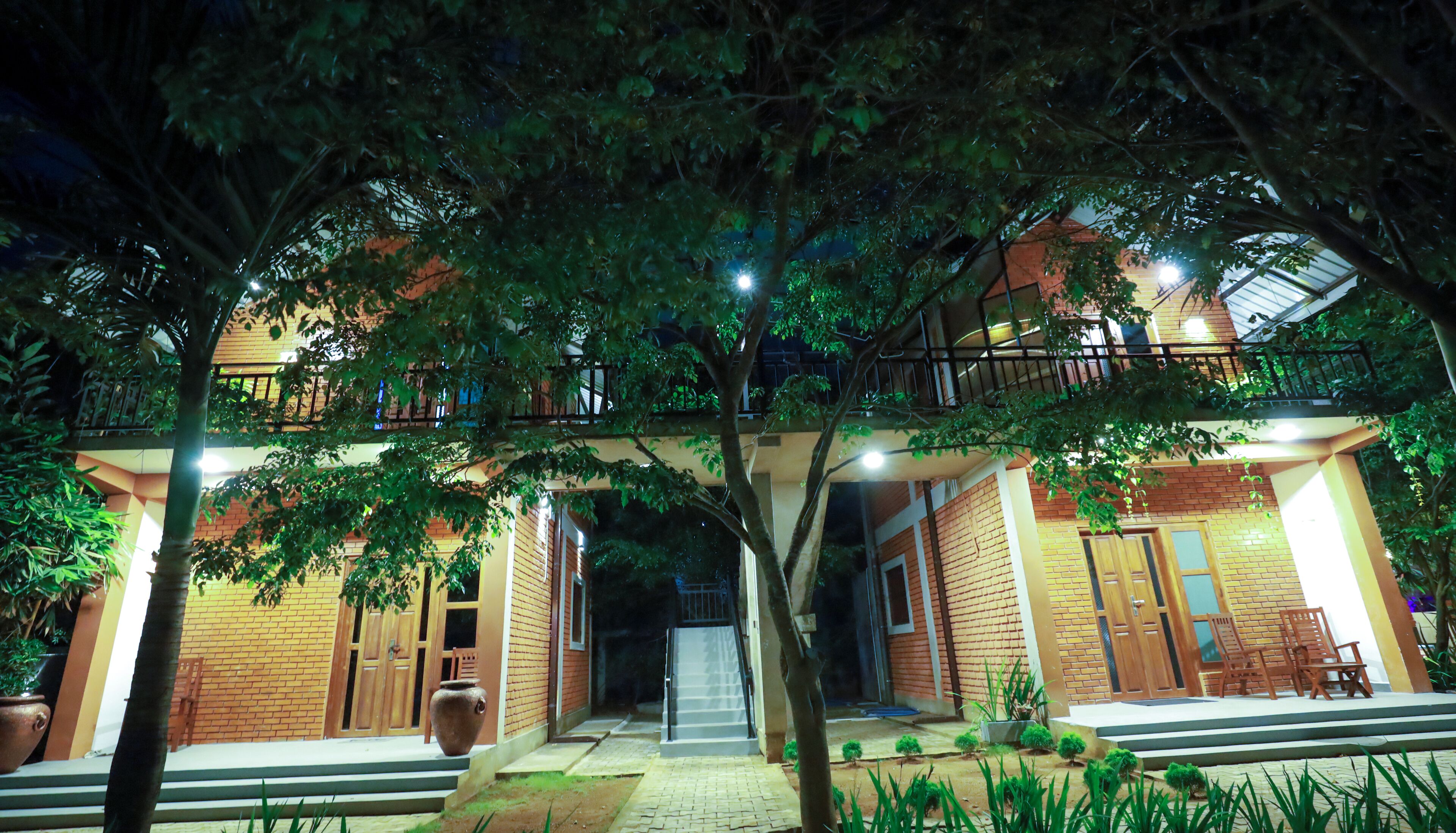 A two-story building with a balcony, a staircase leading to the entrance, and a well-lit outdoor area with potted plants.