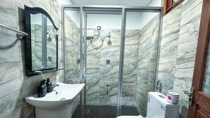 Un bagno con parete in marmo, lavandino, WC e cabina doccia in vetro.