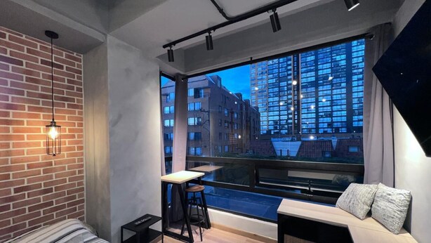 A modern room with a large window, a sofa, a small table, and a stool. - Loft Neoyorquino de Lujo en el Norte de Bogotá, Sauna, Turco, Gimnasio (Bogotá)