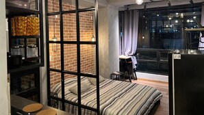 A modern bedroom with a brick wall, a bed with striped bedding, a desk, and a large window with curtains. - Loft Neoyorquino de Lujo en el Norte de Bogotá, Sauna, Turco, Gimnasio (Bogotá)