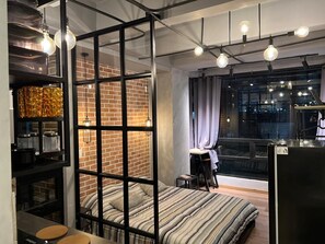 A modern bedroom with a brick wall, a bed with striped bedding, a desk, and a large window with curtains. - Loft Neoyorquino de Lujo en el Norte de Bogotá, Sauna, Turco, Gimnasio (Bogotá)