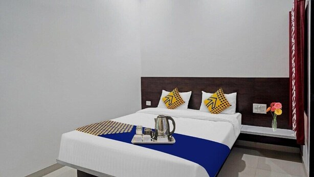 A hotel room with a bed, a bedside table, a nightstand, a vase with flowers, and a coffee maker on the bed. - HOTEL ARAWALI UDAIPUR CITY (Udaipur)