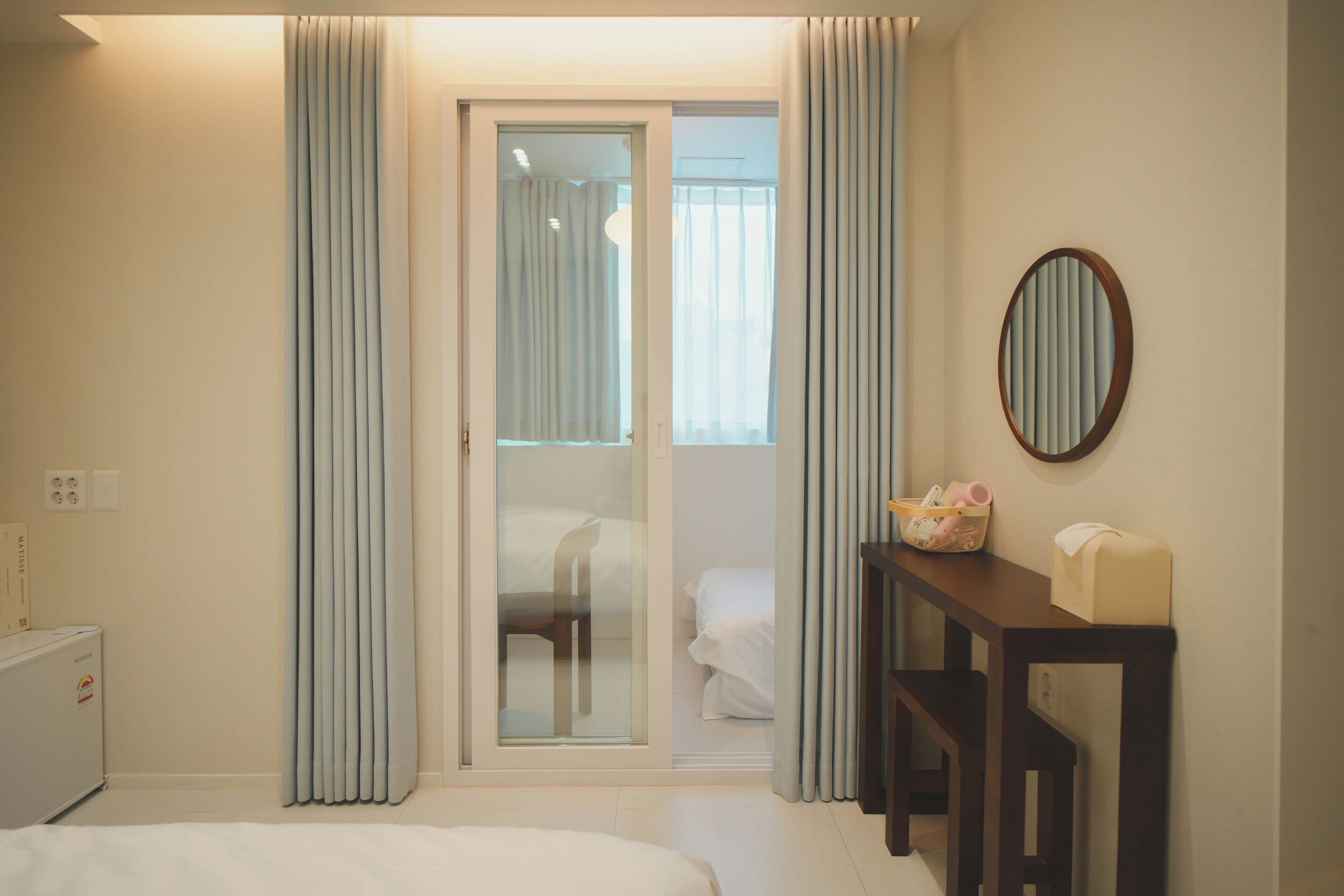 Een hotelkamer met een bed, een bureau, een stoel, een tafeltje, een spiegel en een glazen schuifdeur die leidt naar een balkon.