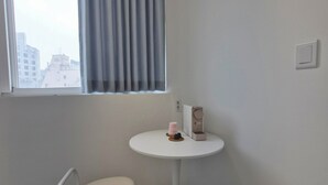Une petite pièce avec une fenêtre, une table blanche sur laquelle se trouve une machine à café, et deux chaises, une jaune et une blanche.