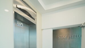Un ascenseur orné d’une pancarte indiquant « Restez élégant, restez le bonjour », doté d’un sol carrelé et d’une porte donnant sur une autre pièce.