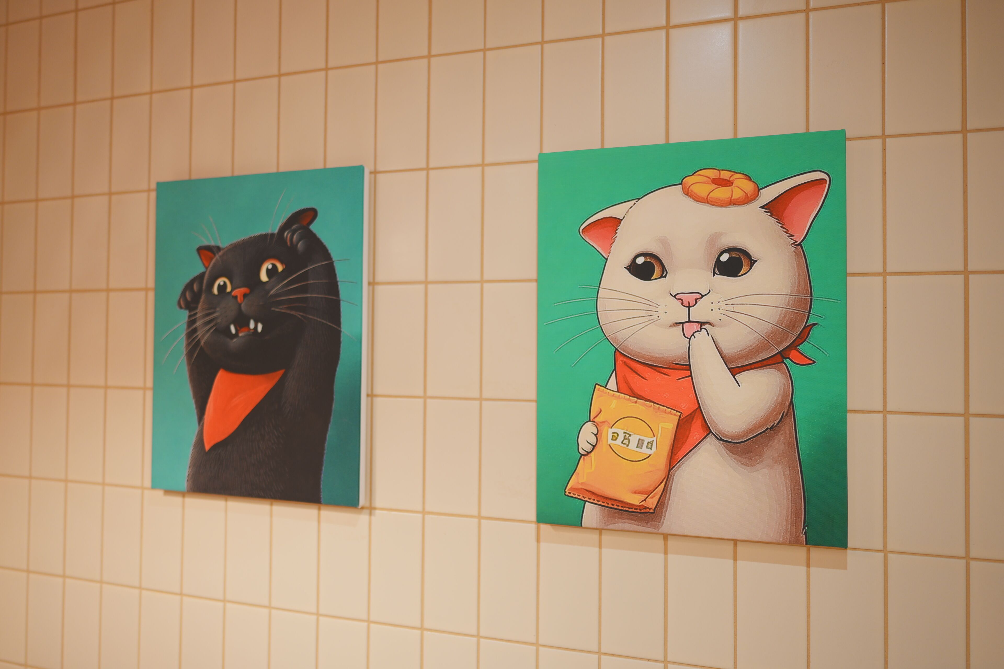 Deux peintures représentant des chats de dessin animé sur un mur carrelé.