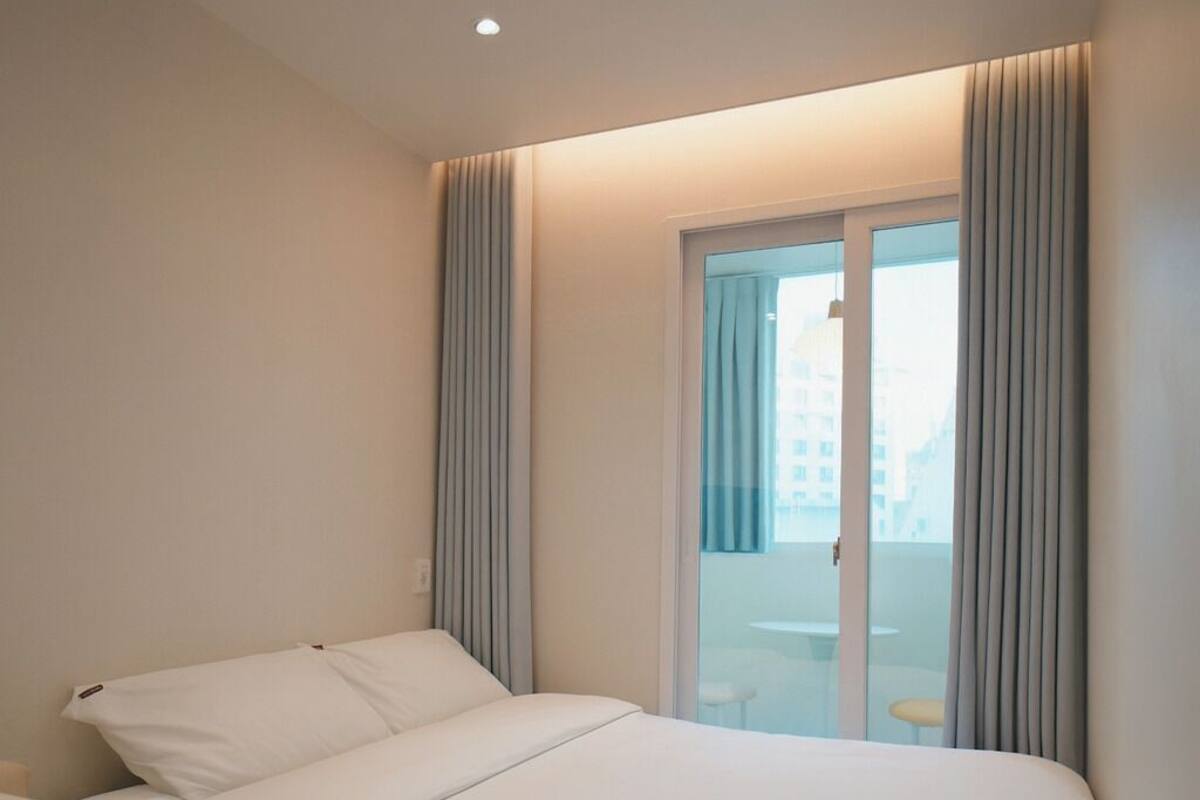 A hotel room with a bed, a chair, a window with curtains, and a view of the city.