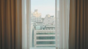 Une vue à travers une fenêtre avec des rideaux, donnant sur un paysage urbain avec de nombreux bâtiments.