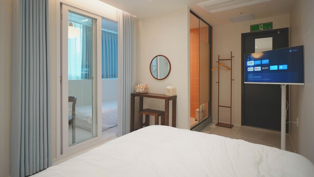 Une chambre d’hôtel équipée d’un lit, d’une télévision, d’un miroir et d’une porte coulissante donnant sur un balcon.