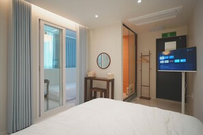 Une chambre d’hôtel équipée d’un lit, d’une télévision, d’un miroir et d’une porte coulissante donnant sur un balcon.