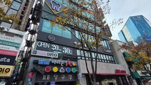 Un immeuble à plusieurs étages, orné de diverses enseignes commerciales, notamment un magasin d’informatique et un café.