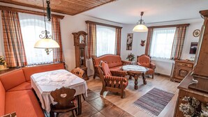 A cozy room with a wooden ceiling, a dining table with chairs, a sofa, a clock, and a cabinet. - Beautiful apartment for 2 guests with WIFI and TV (Michaelerberg)