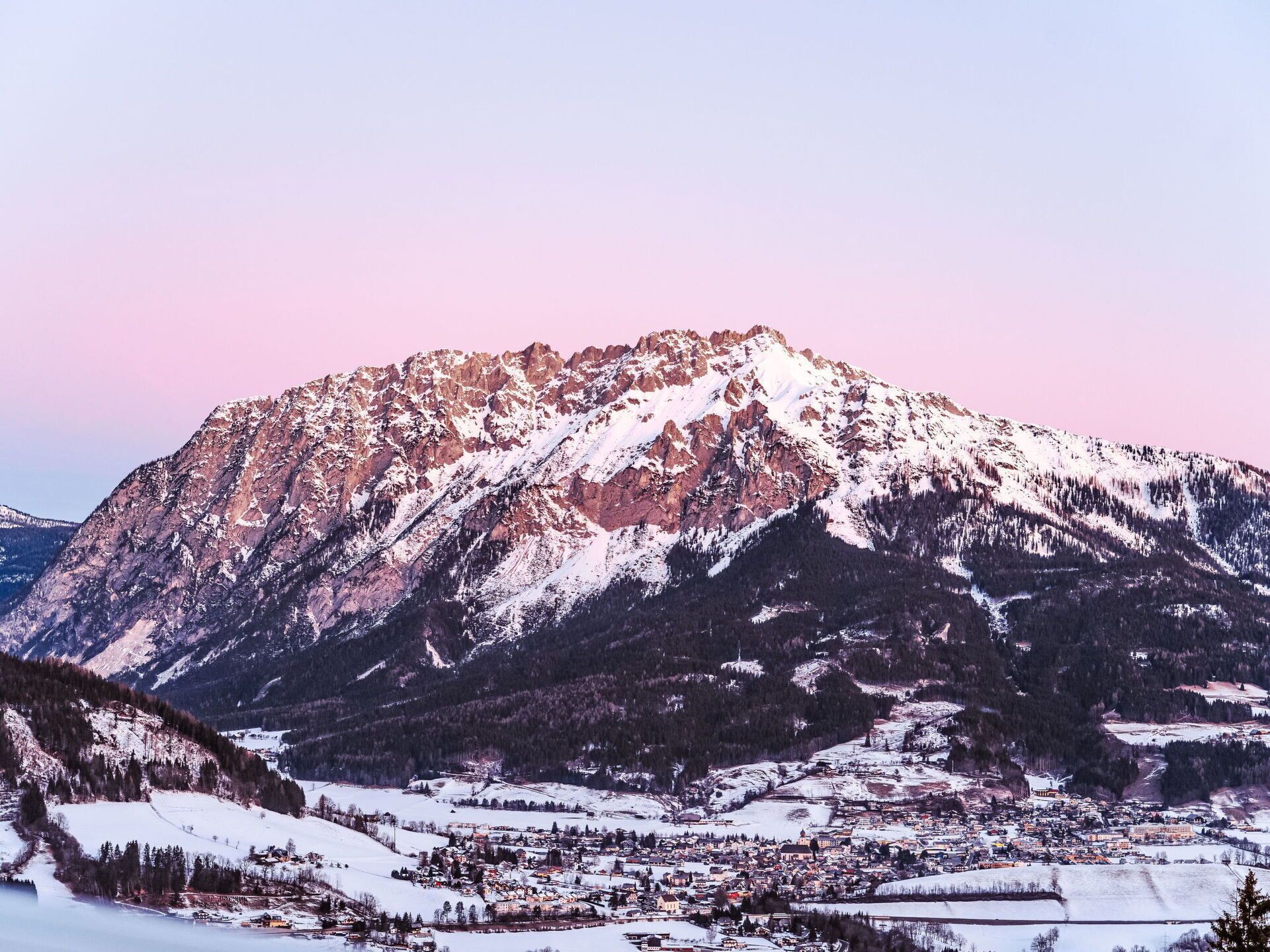 Una montaña con un pueblo en su base, rodeada de terreno nevado.