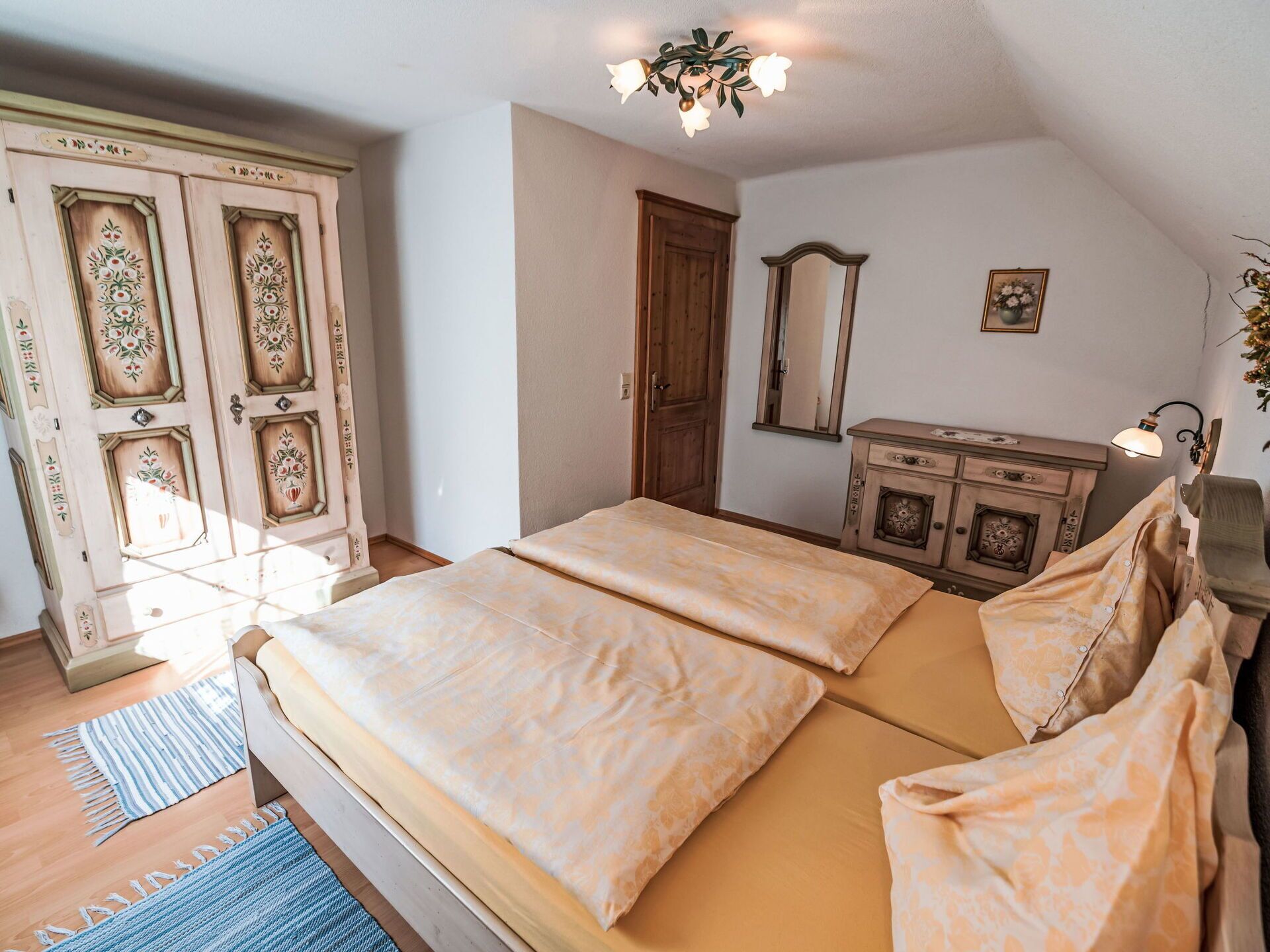 Un dormitorio con cama, cómoda, espejo y puerta con paneles decorativos.