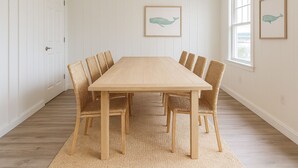 Comedor con mesa de madera y sillas de mimbre, paredes blancas con paneles y ilustraciones enmarcadas de ballenas.