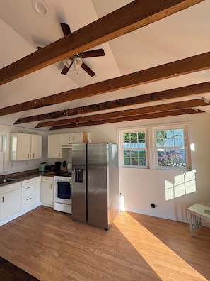 Una cocina con vigas de madera, un refrigerador de acero inoxidable, una estufa y una ventana con vistas al verdor.
