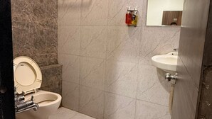 A bathroom with a toilet, bidet, sink, and a mirror. - HOTEL LOTUS (Surat)