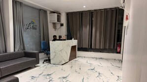 A modern hotel lobby with a marble floor, grey sofa, and a reception desk. - HOTEL LOTUS (Surat)