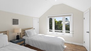 Ein Schlafzimmer mit zwei Betten, einem Fenster mit Blick auf Palmen, einem Deckenventilator und einem Wandlüfter.
