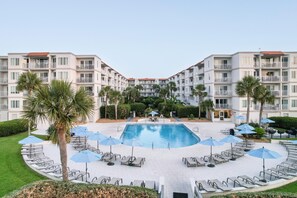 Ein Hotel mit einem zentralen Schwimmbecken, umgeben von Liegestühlen und Sonnenschirmen, mit mehreren Etagen und Balkonen.