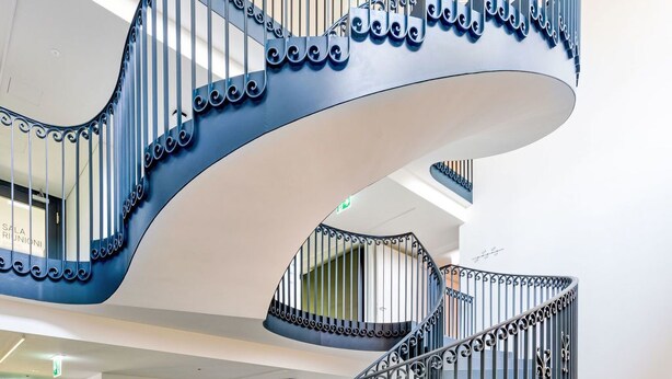Eine Wendeltreppe mit aufwändig gestalteten schwarzen Geländern in einem modernen Gebäude.