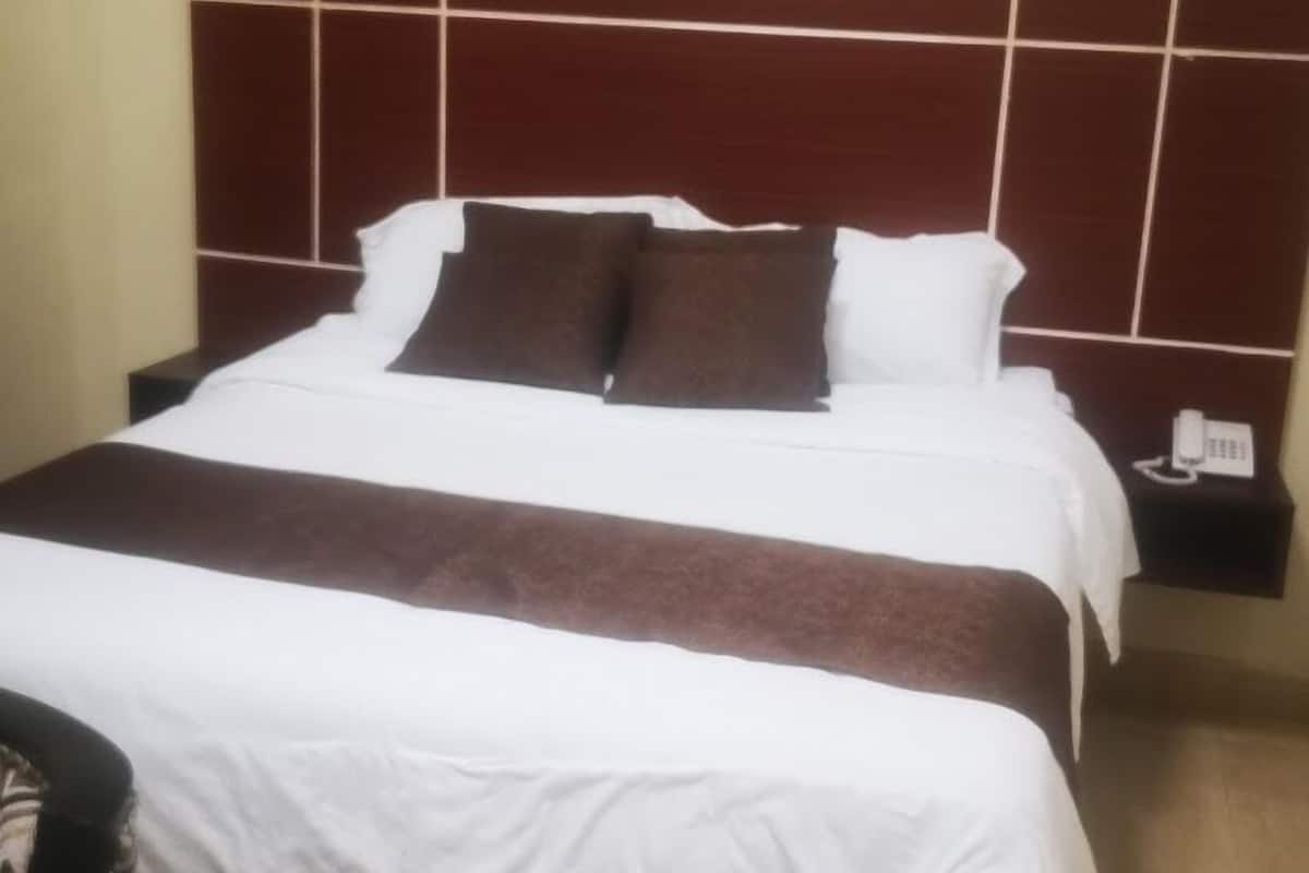 A hotel room with a large bed, a nightstand with a phone, and a wall-mounted light fixture.