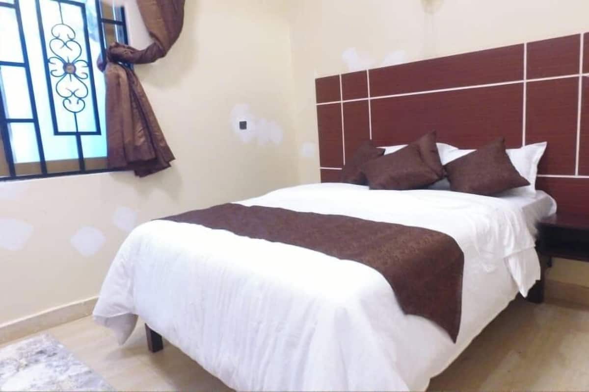 A neatly made bed with a white and brown bedspread, a headboard with a grid pattern, and a window with curtains.