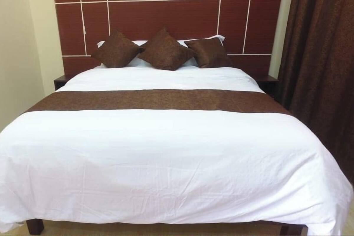 A neatly made bed with white and brown bedding, a wooden headboard, and a plain wall.