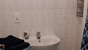 Kylpyhuoneessa on valkoinen pesuallas, peili, pyyhekoukku, pieni jakkara ja pesukone.