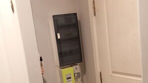 Kapea käytävä, jonka oikealla puolella on valkoinen ovi, vihreä kaappi ja valkoinen seinä, jossa on termostaatti.