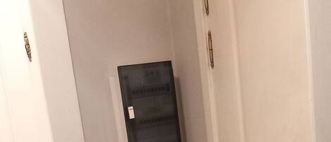 A narrow hallway with a white door on the right, a green cabinet, and a white wall with a thermostat.