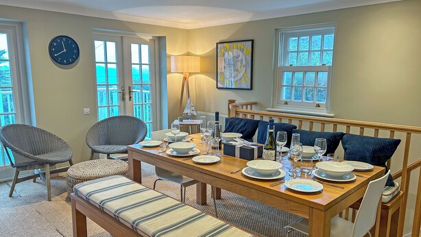 A dining area with a wooden table set for four, surrounded by wicker chairs and a bench. - Reverse-level retreat in St Mawes, perfect for family or friends. (St Mawes, near Falmouth)