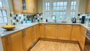 A kitchen with wooden cabinets, a granite countertop, a sink, and a window with a view of trees. - Reverse-level retreat in St Mawes, perfect for family or friends. (St Mawes, near Falmouth)