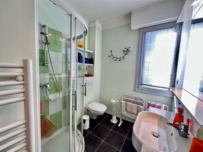 Ein Badezimmer mit Duschkabine, Toilette, Waschbecken und Fenster.