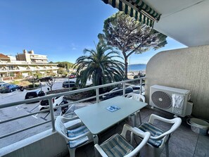 Un balcón con mesa y sillas, vista al mar, una palmera y edificios al fondo.